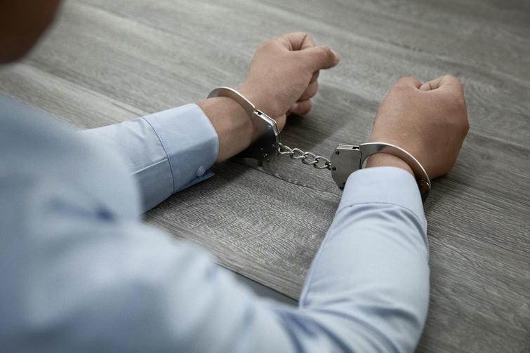 selective-focus-shot-of-male-hands-in-handcuffs-on-a-wooden-table_181624-57683