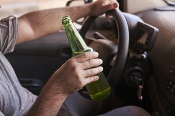 bottle-of-beer-in-a-man-s-hands-driving-the-car-during-daytime_181624-46717