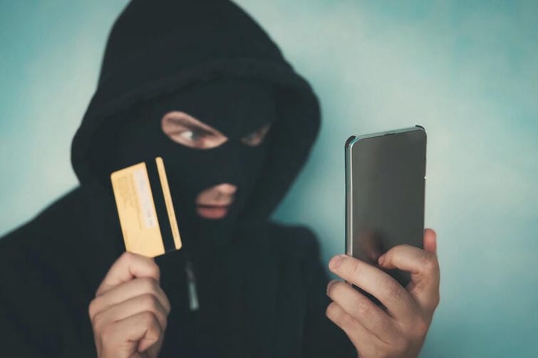 close-up-of-a-man-in-robbery-mask-and-hood-holding-the-credit-card-and-looking-at-the-smartphone-screen-male-criminal-arranges-a-financial-affair-with-mobile-and-credit-card-network-fraud-dangers_431724-1825